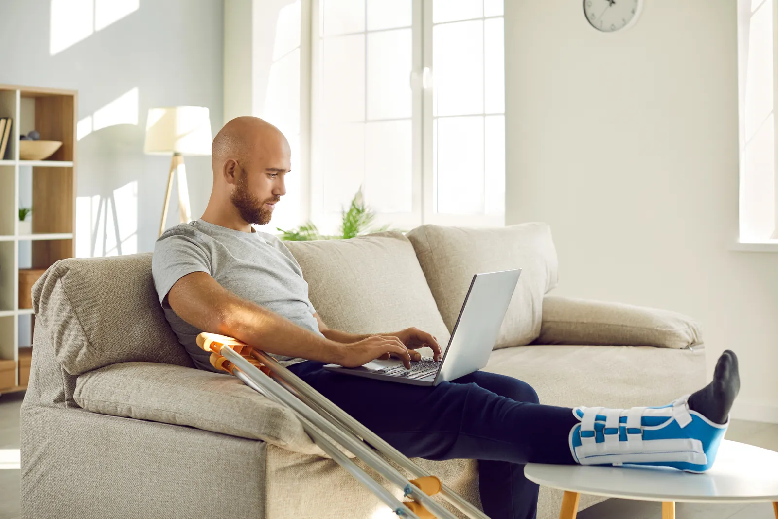 An injured worker uses a laptop at home with crutches nearby — managing ill or injured employees in Australia