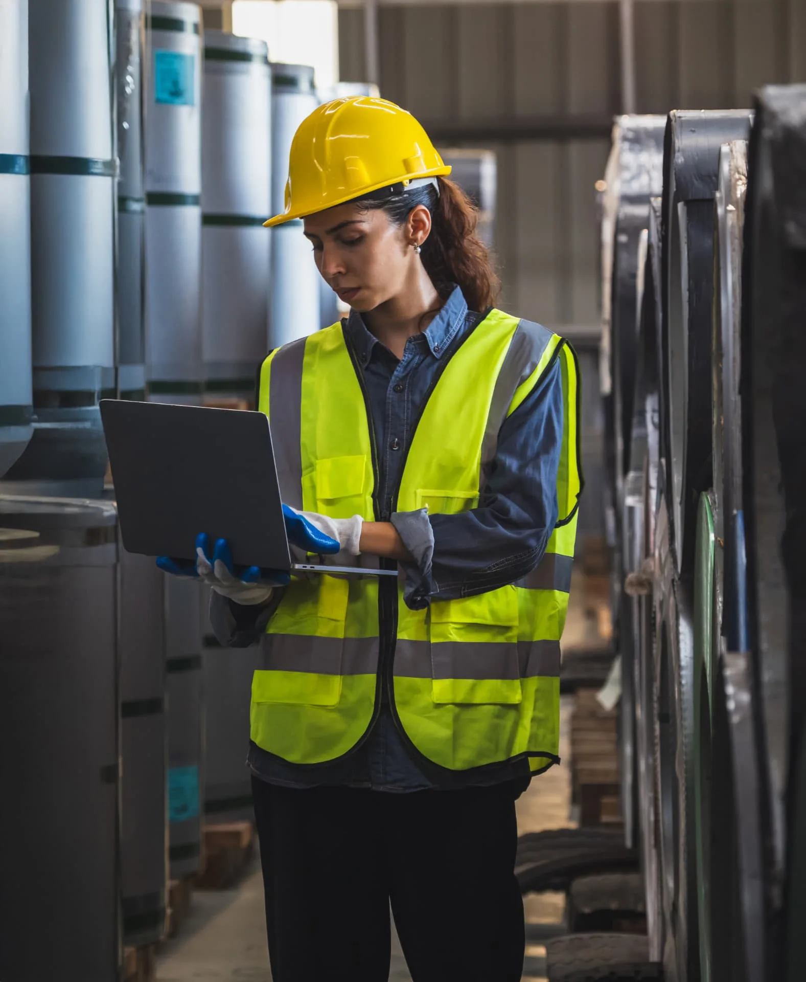 A worker in a hard hat and high-visibility vest using a laptop in a warehouse