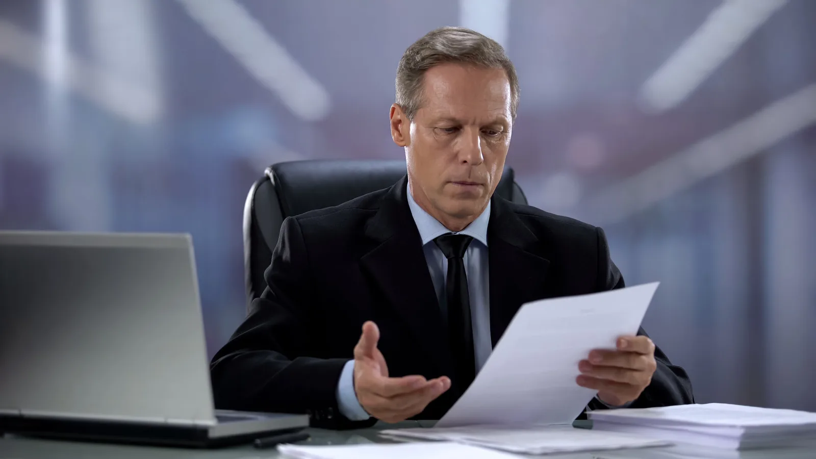 A businessman reviewing documents at a desk beside a laptop