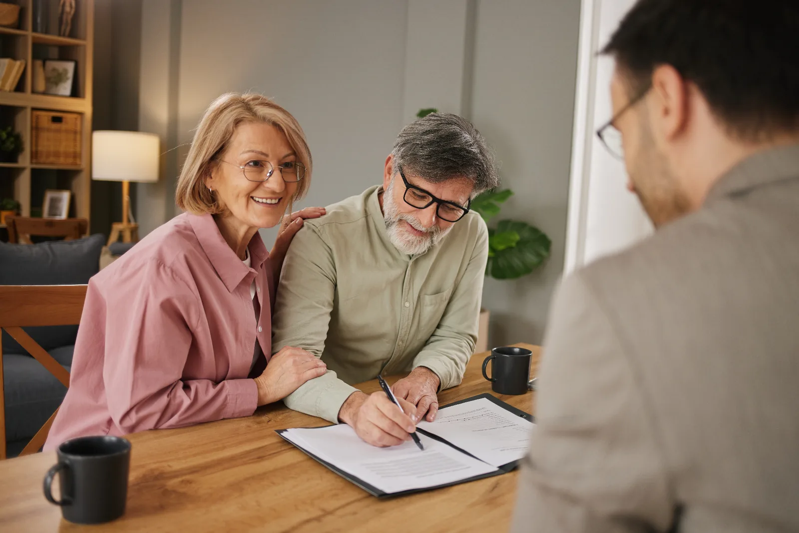 Older man signing documents at a table with an adviser and another adult