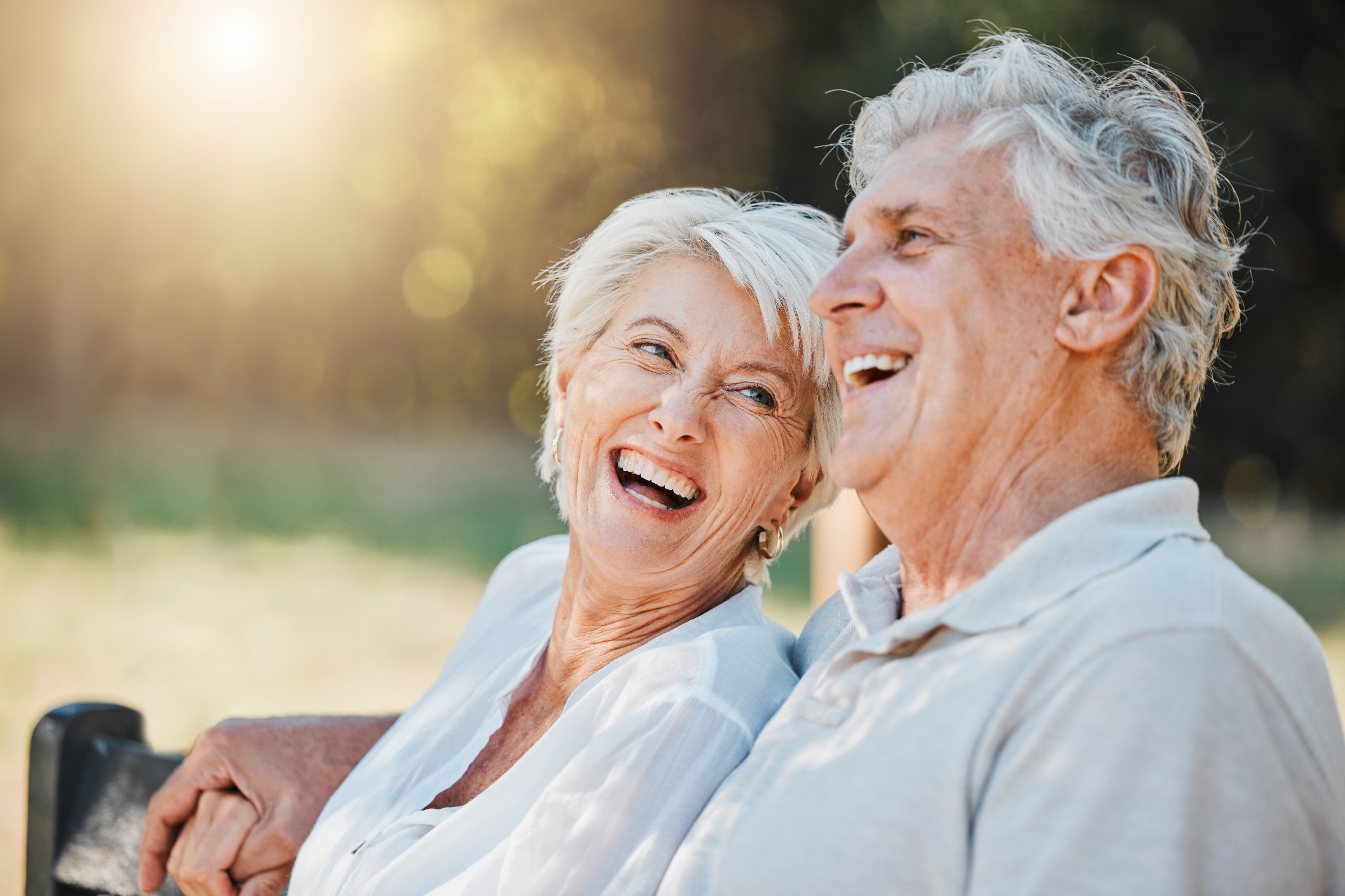 Older man and woman laughing together on a park bench in warm afternoon light