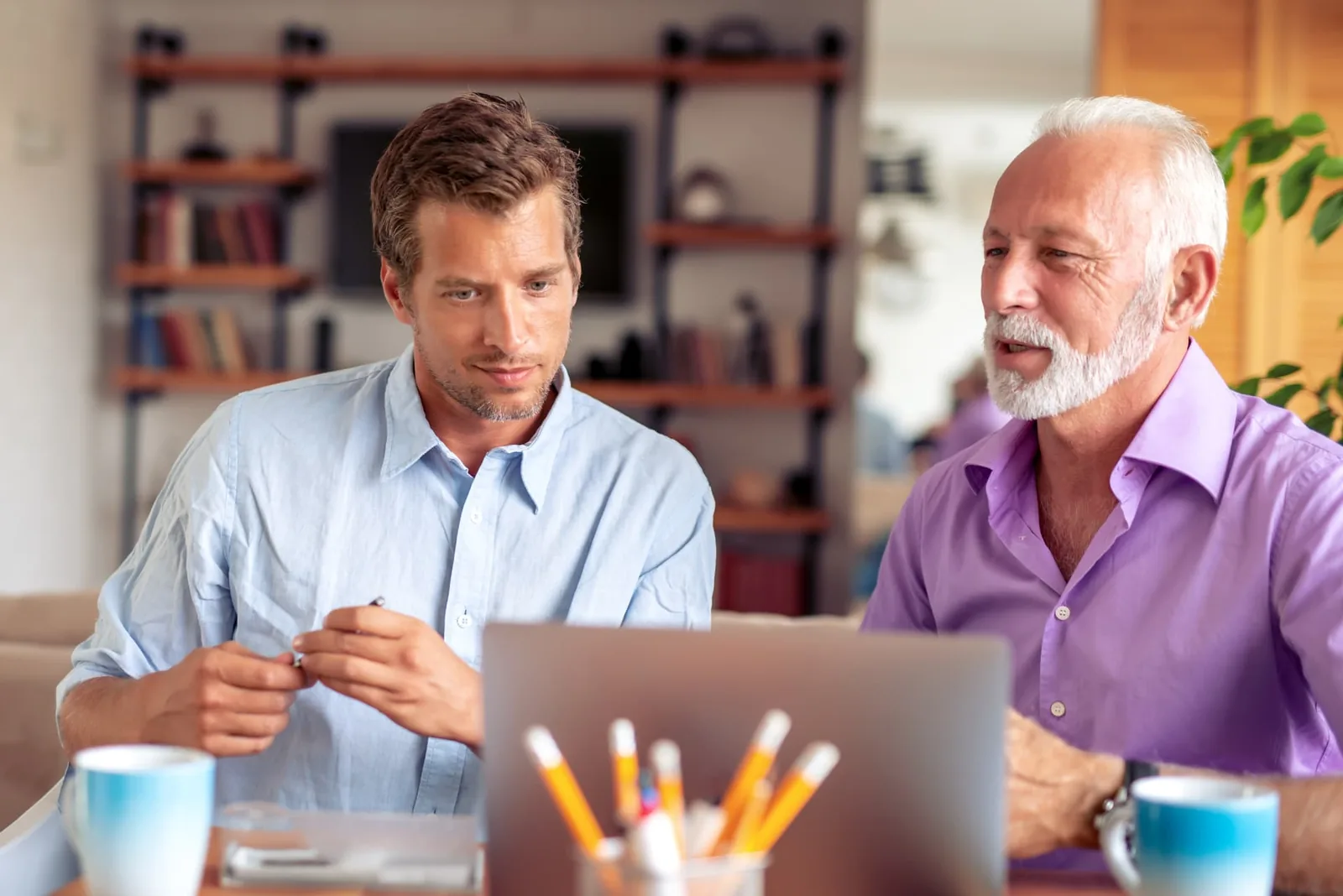 Two men discussing documents beside a laptop