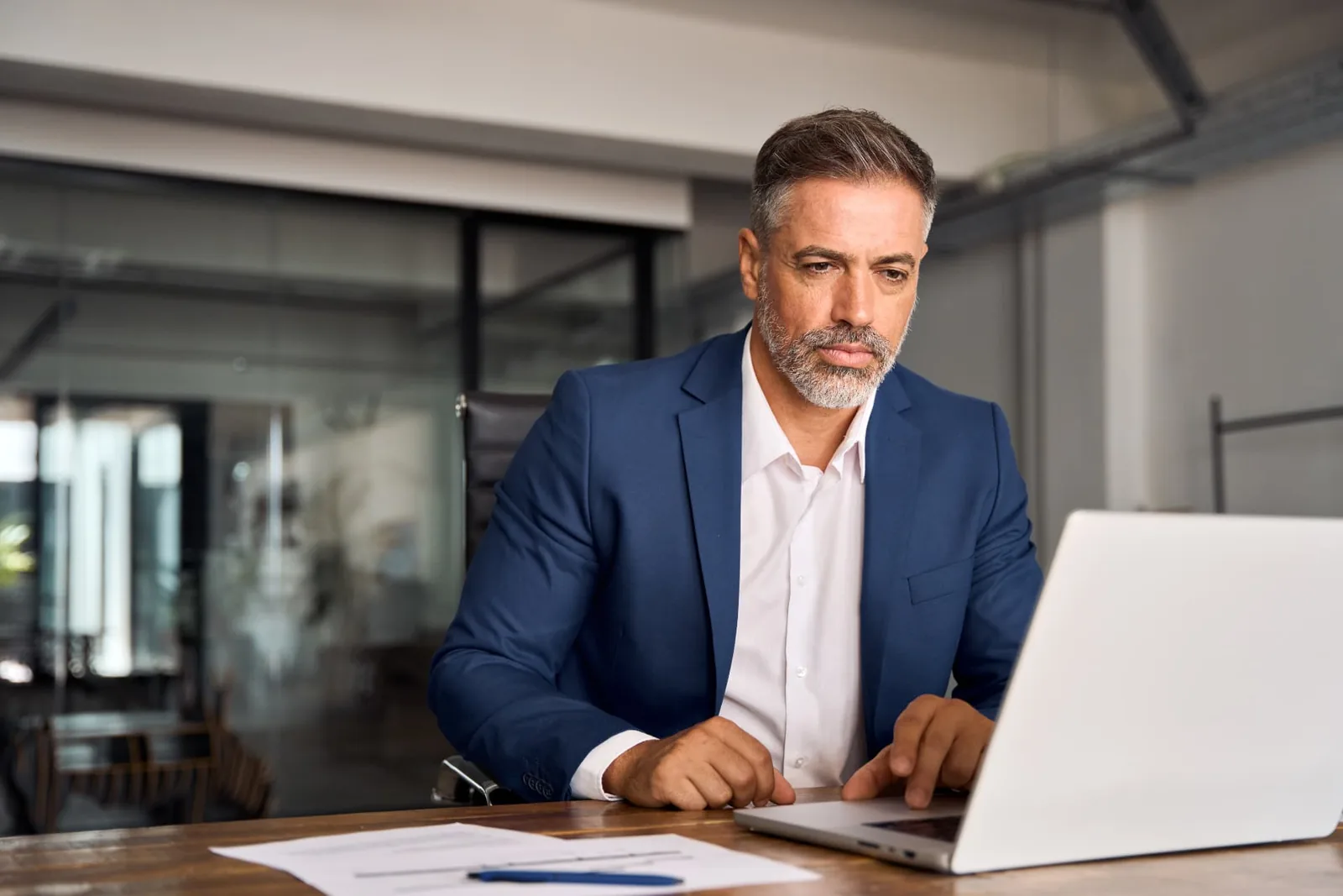 A man examining documents beside a laptop in an office