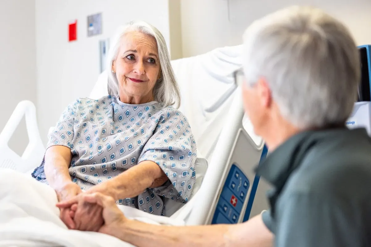 An older woman in a hospital bed holding hands with a loved one